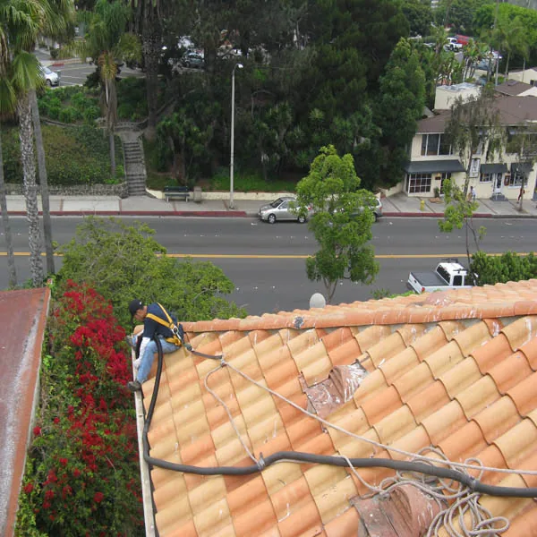 Technician working on a tile roof during roof-level gutter cleaning.